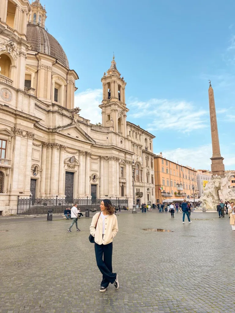 Woman walking in Piazza Navona, Rome, with historic Baroque buildings and fountain in the background.