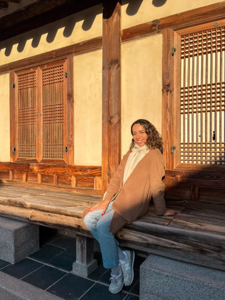Woman sitting down infront of a hanok on the grounds of the Gyeongbokgung Palace with unique wood work on the windows.