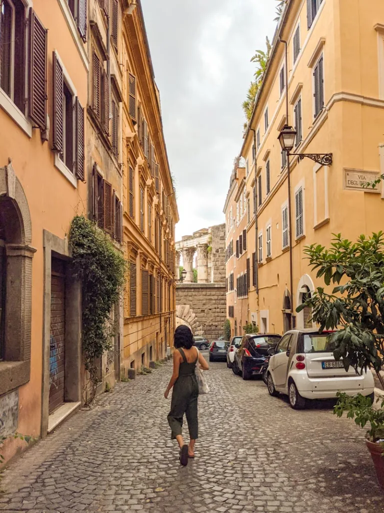 Woman walking down a quiet cobblestone street in Monti with a view of the Colosseum at the end.