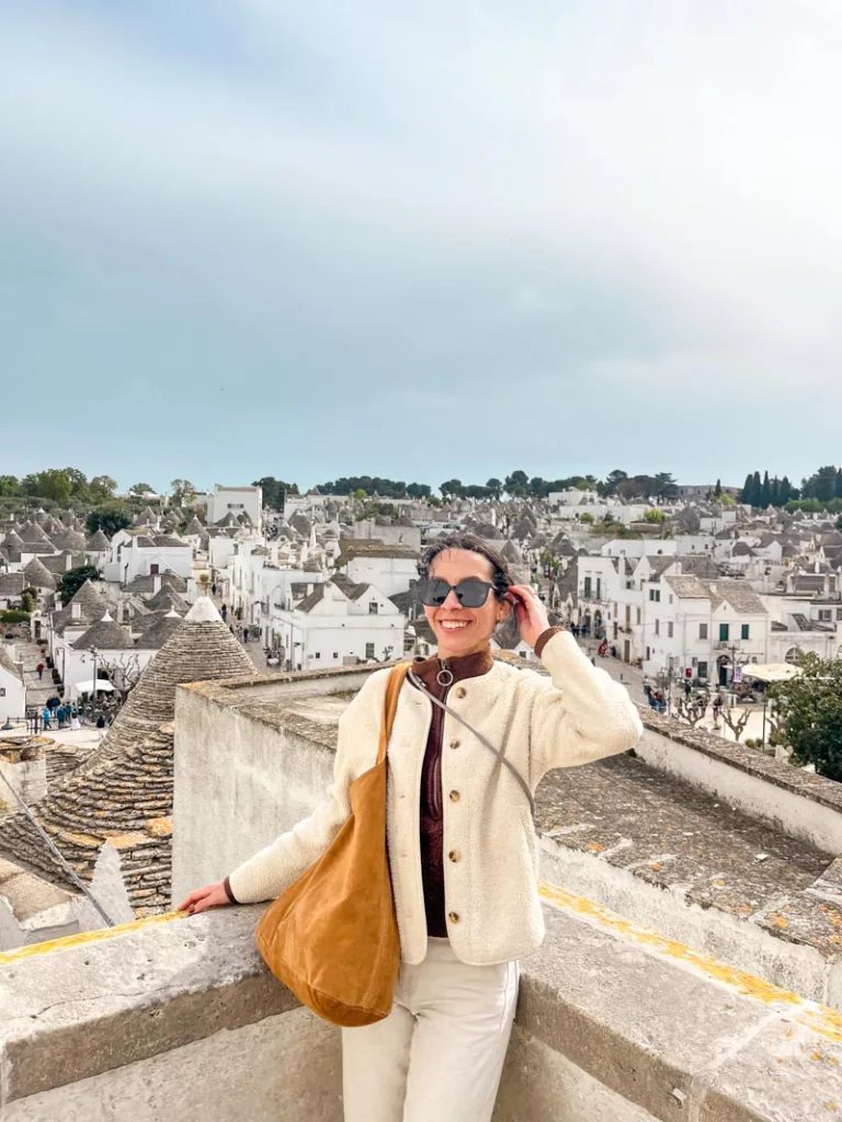 woman smiling from a viewpoint overlooking the trulli roofs of alberobello