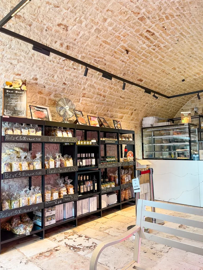 inside the la lira focacceria shop in alberobello, with a display of local products for sale on a black shelf