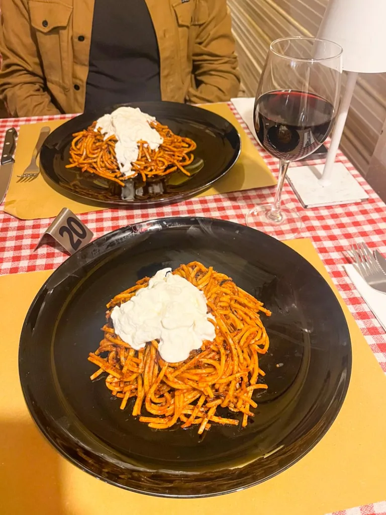 two big plates of spaguetti a l'assasina, and a glass of red wine, on a table with a red checkered table cloth at Anto Ristorante Cucina Tipica Pugliese in bari