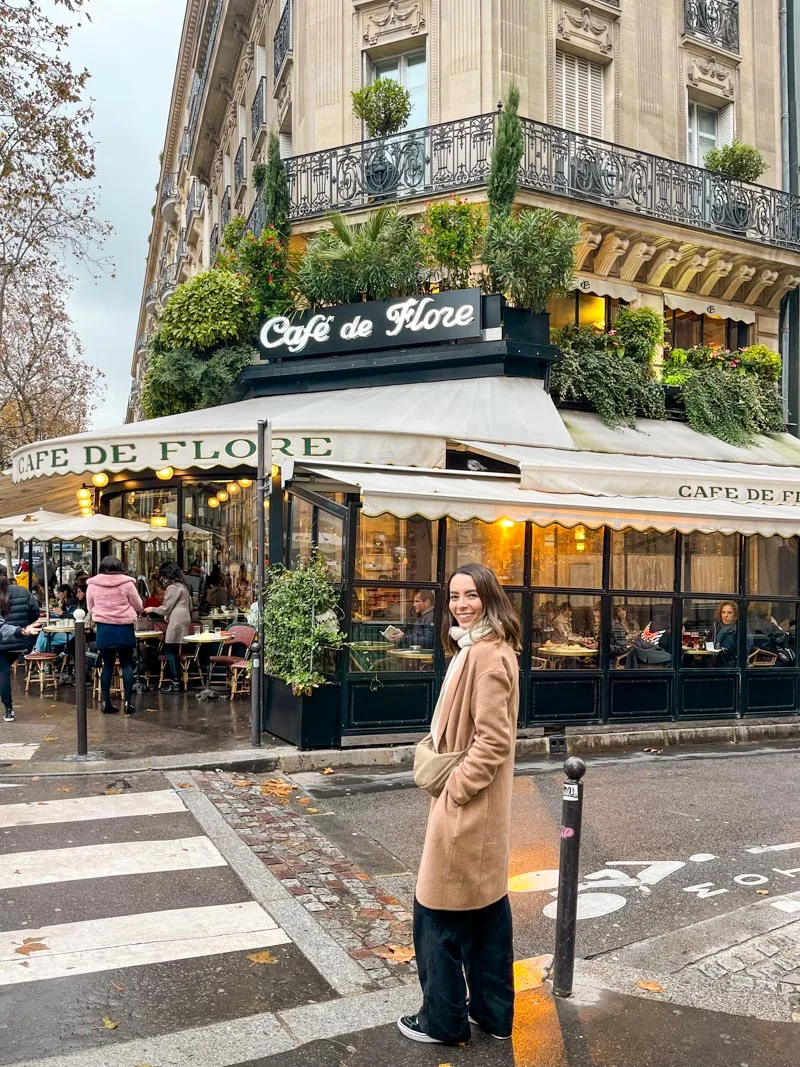 woman standing in front of cafe de flore in paris smiling at the camera