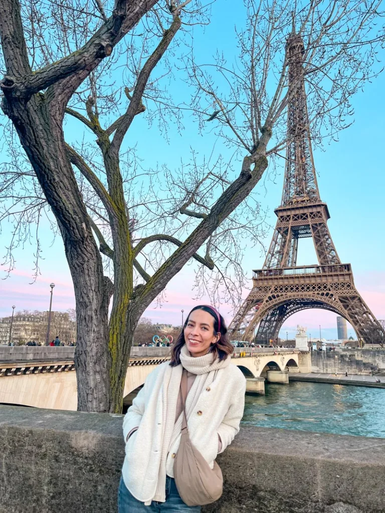 woman smiling, across the seine, with a view of eiffel tower and cotton candy colored skies in the back