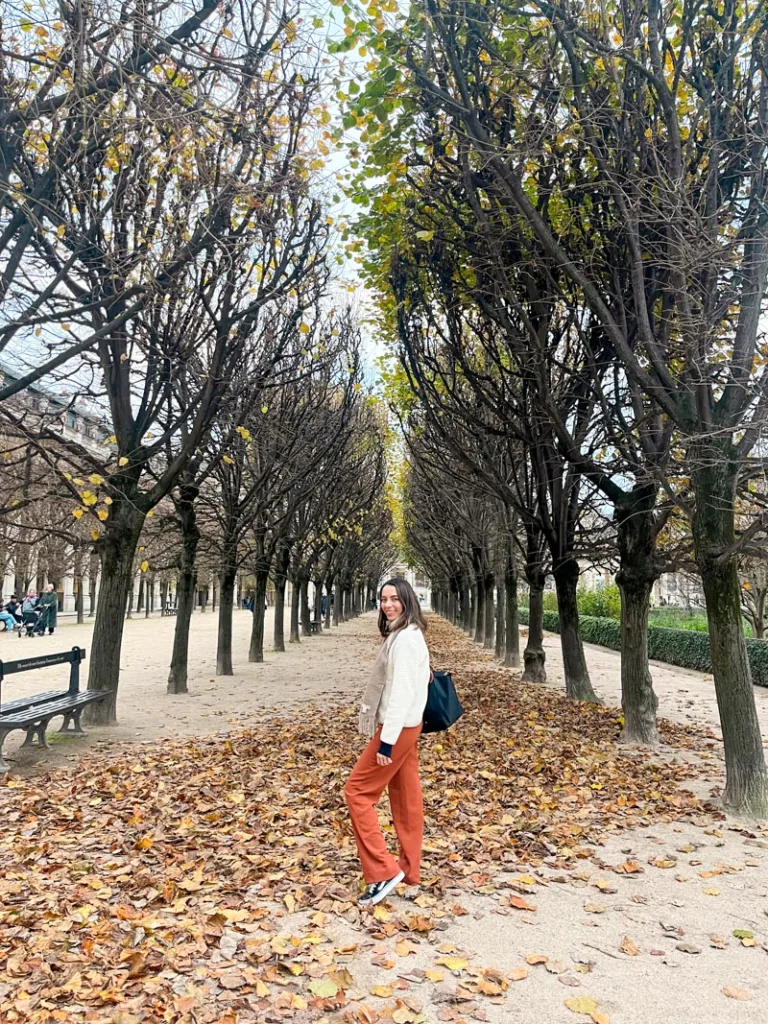 woman standing on a walkpath covered in fallen autumn leaves at jardin du palais royal