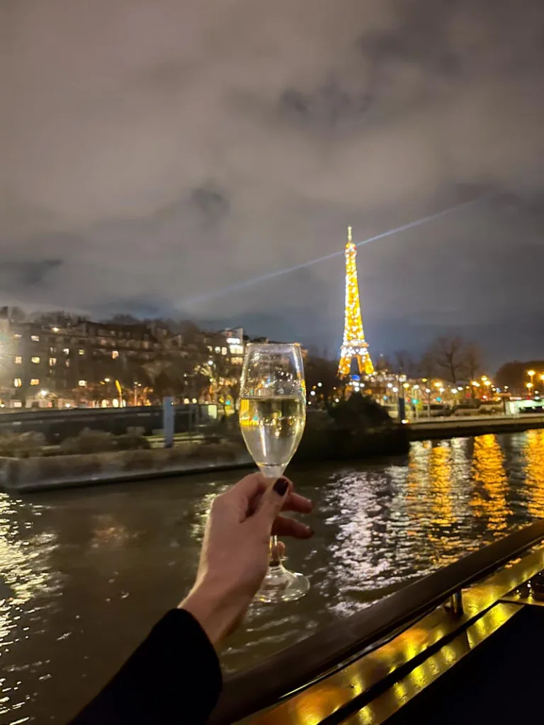 hand holding a champagne glass from a sine river cruise with a view of the eiffel tower sparkling in the back