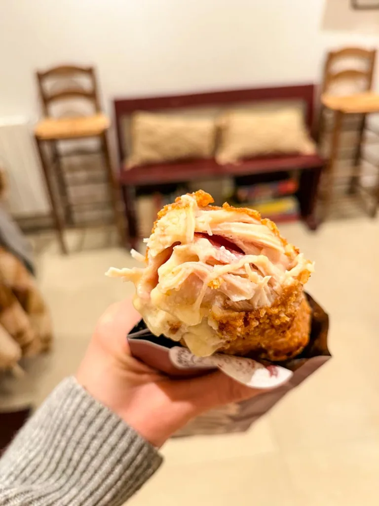 hand holding a cordon blue roll with melted cheese coming out of it at amone restaurant in paris