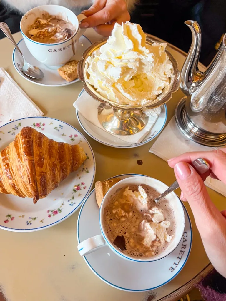 two cups of hot chocolate, a mountain of whip cream on a bowl, and a croissant at carette in le marais