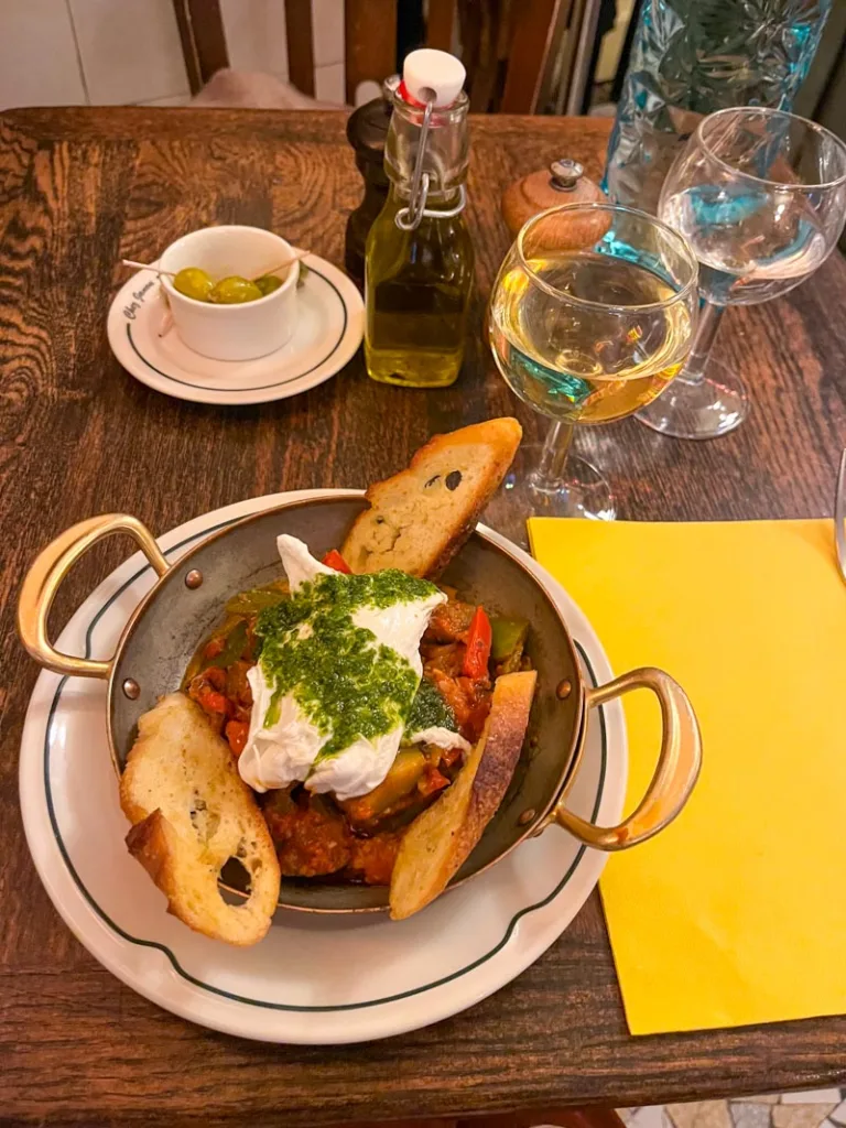 a ratatouille plate, a small bowl with olives, a glass of white wine, and a glass of water on a table at chez janou
