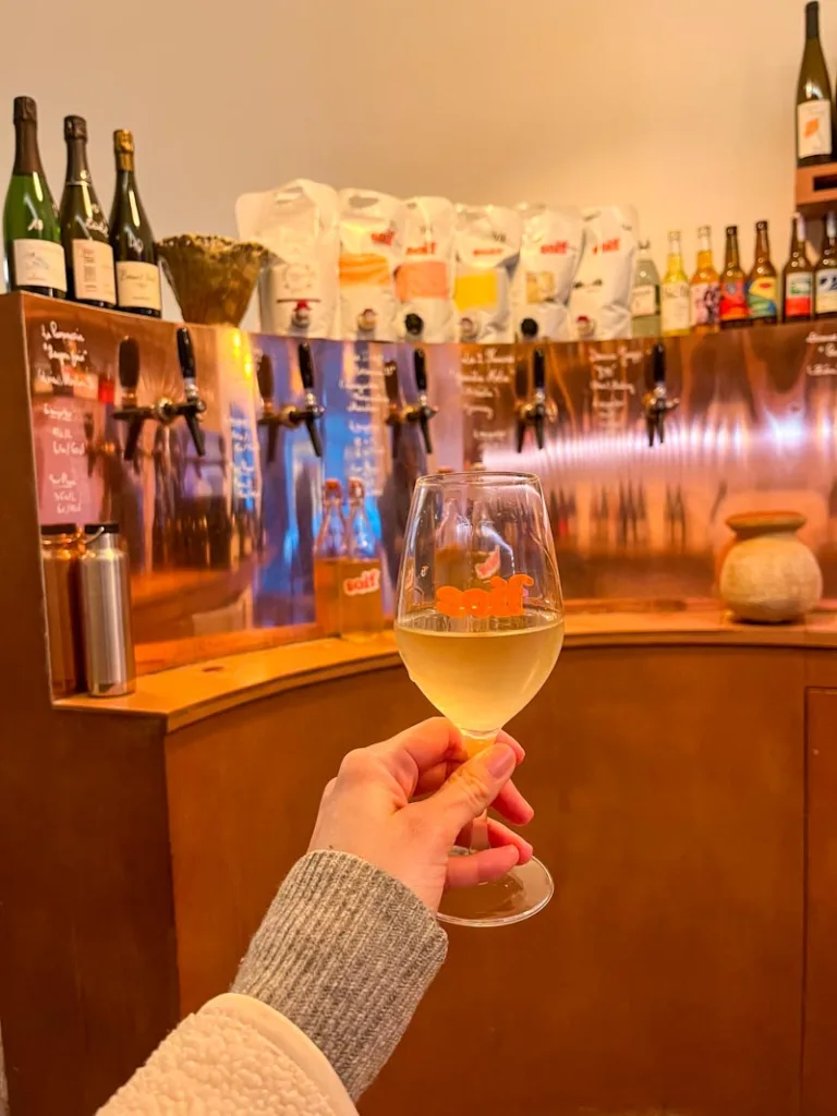 hand holding a glass of wine with a rose gold bar at the back with wine on tap at soif in paris