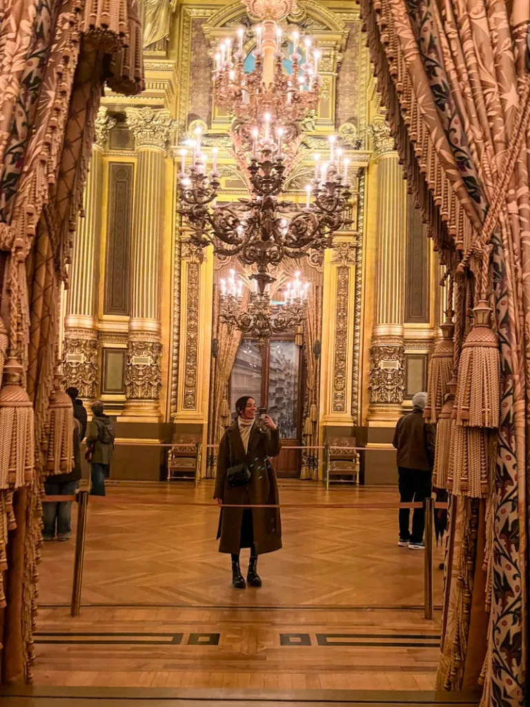 woman taking a selfie on one of the mirrors inside the grand foyer at palais garnier in paris