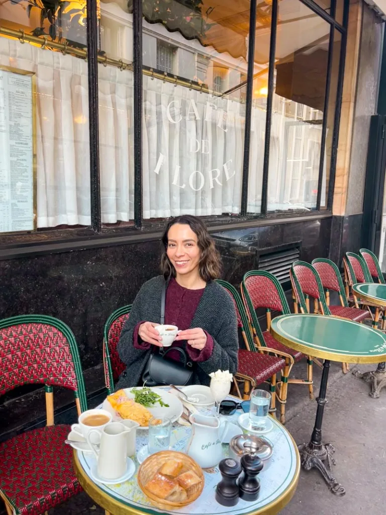 woman sitting at an outdoor table at cafe de flore holding a cup of hot chocolate