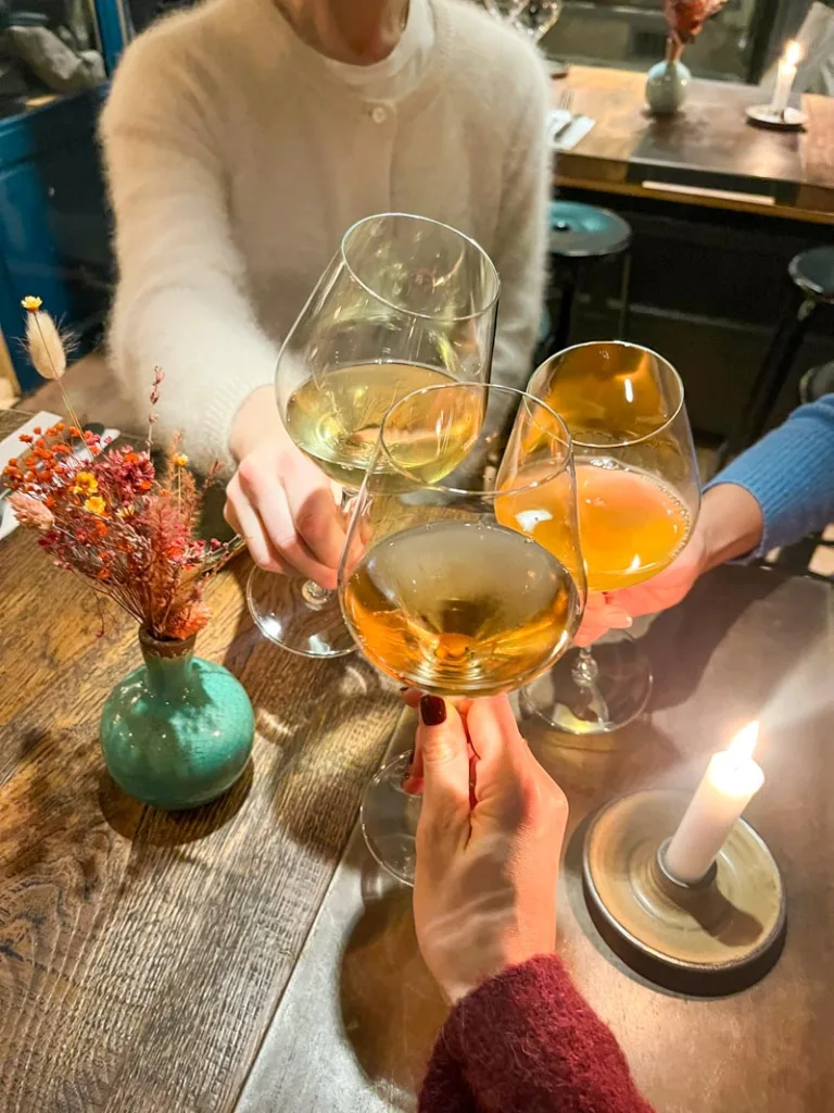three hands holding a glass of wine cheering at the center of the table at la grande cremerie in saint germain des pres in paris