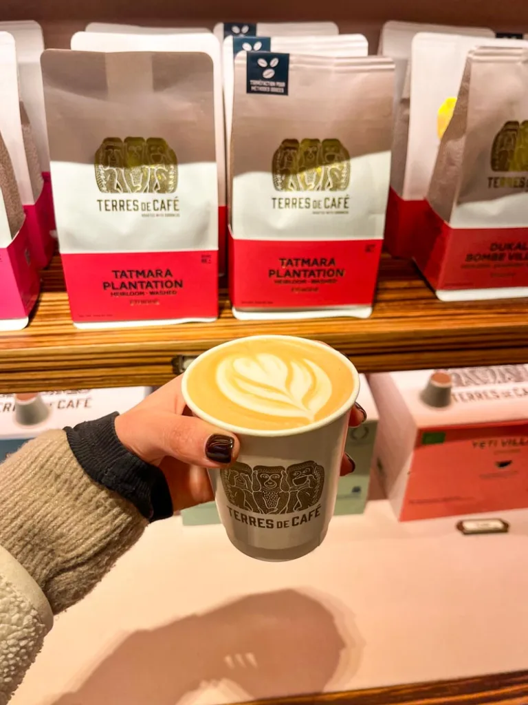 hand holding a latte in a to go cup from terres de cafe in saint germain des pres, paris