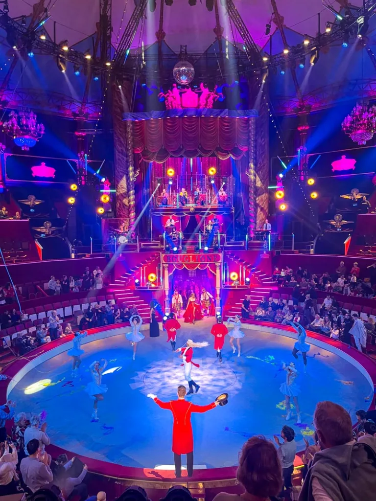 view of a circus ring with a ring master at the center, and dancers around, at circus bouglione in paris