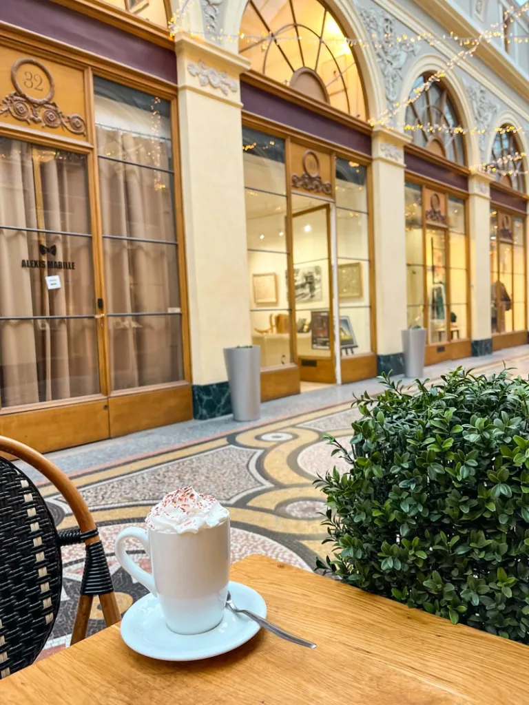 a cup of hot chocolate on a wooden table inside the galerie vivienne in paris