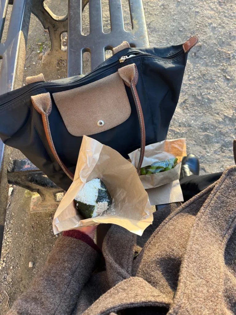 an onigiri, a bag of edamame, and a womans hand bag on a bench at jardin du palais royal in paris