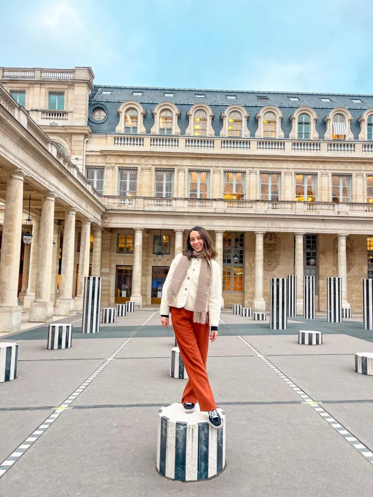 woman standing on one of the black and white colonnes de buren at the domaine du palais royal in paris