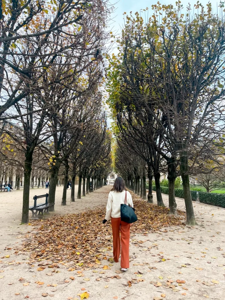 woman walking through a tree lined promenade at the jardin du palais royal