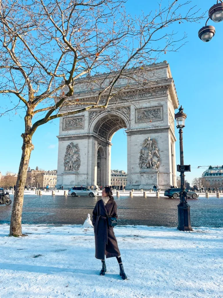woman standing in front of the arc de triomphe in paris on a snowy day
