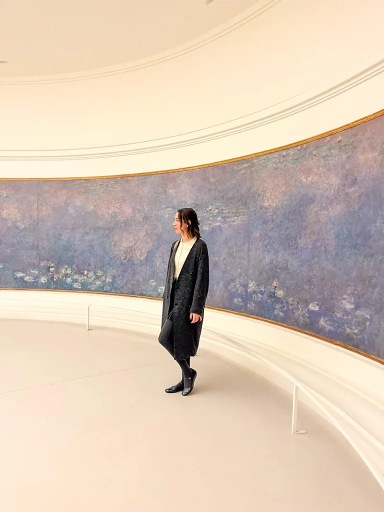 woman standing in front of a curved wall displaying monet's big water lilies painting at musee de l'orangerie