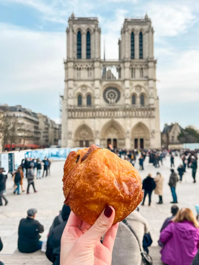 hand holding a pain au chocolat infront of the notre dame cathedral