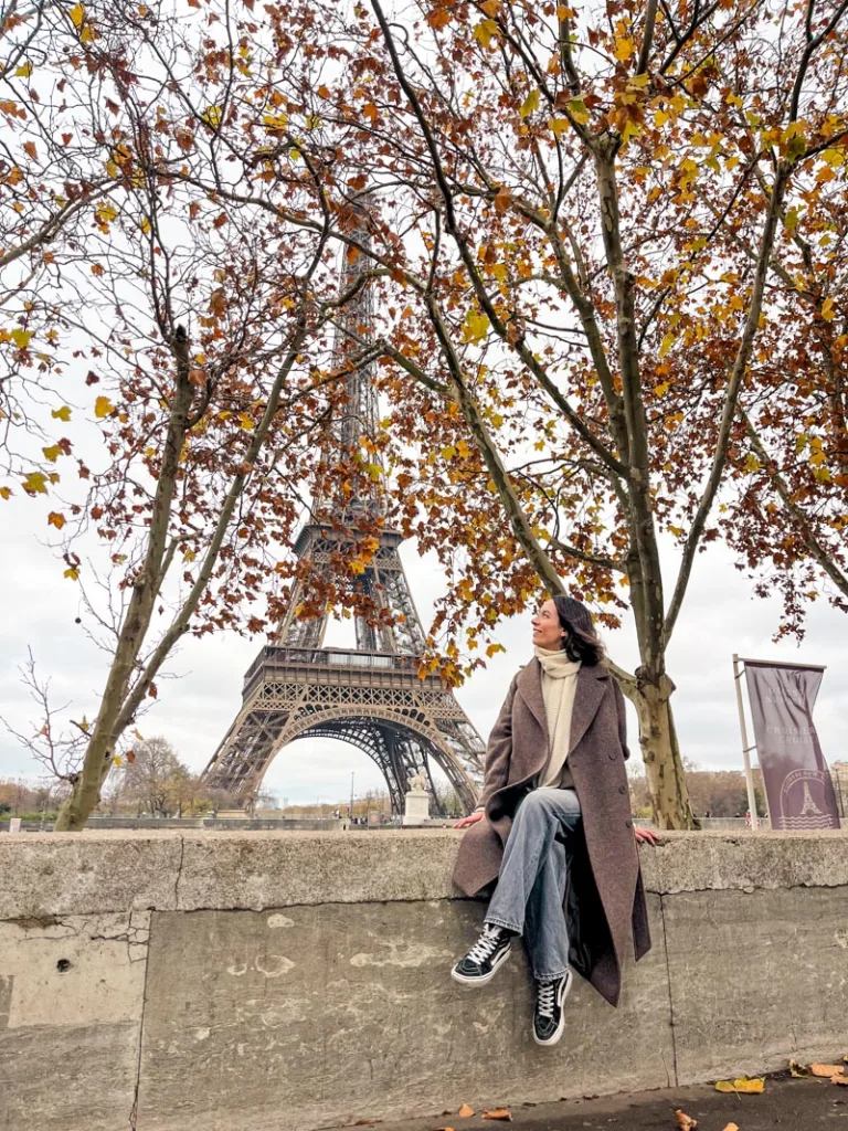 Woman sitting near the Eiffel Tower in Paris framed by autumn trees