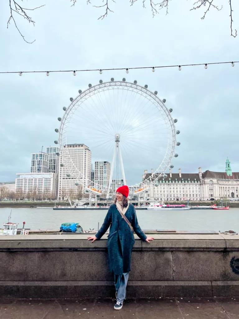 woman standing in front of the london eye across the river