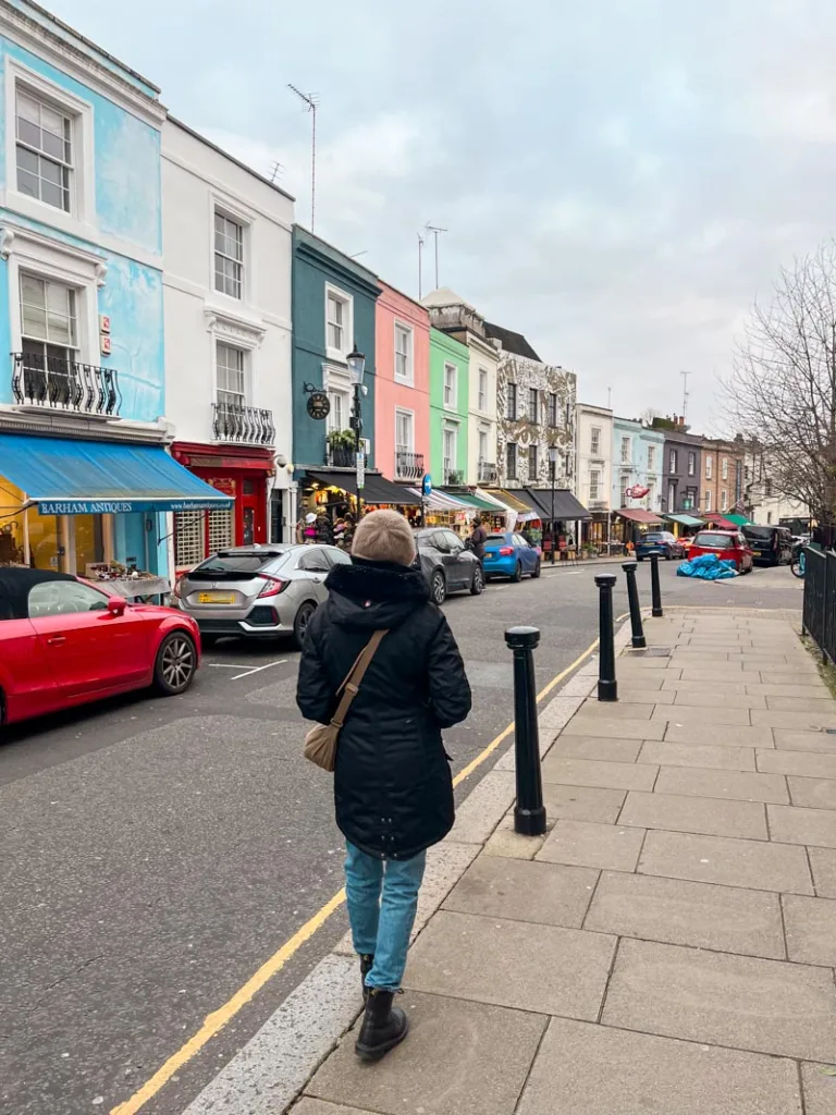 woman walking along the street lined with colorful houses at portobello road market in london