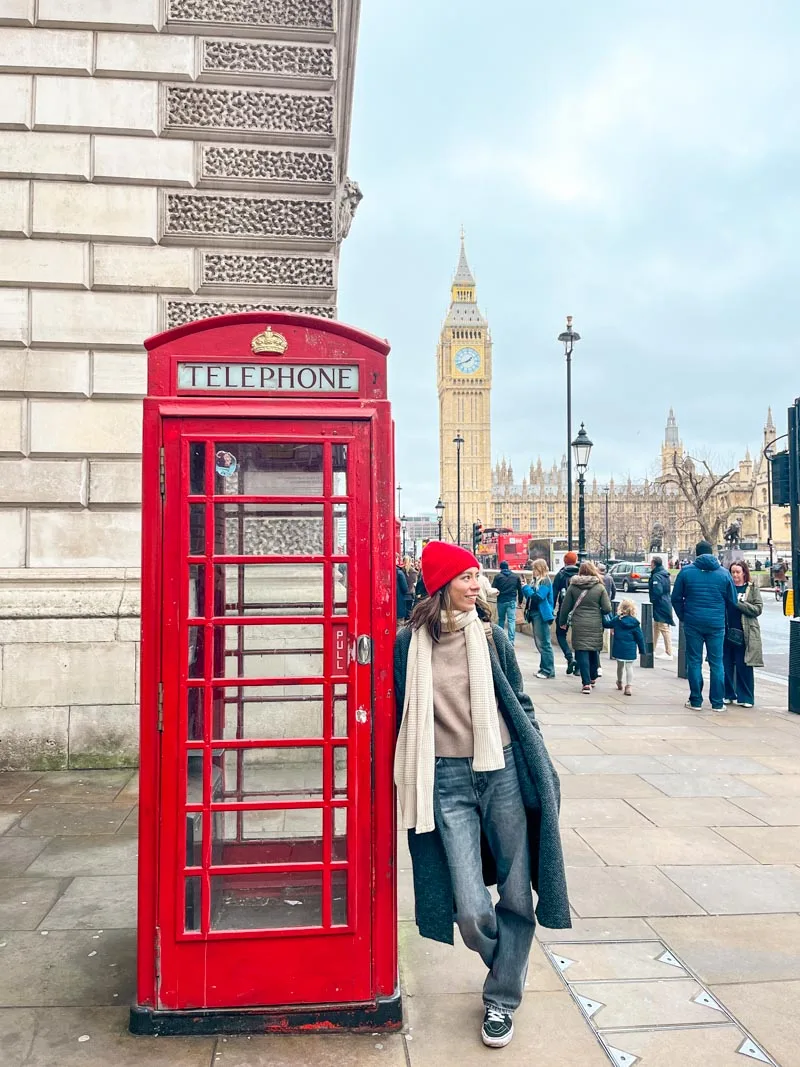 woman standing next a red phone booth in london with a view of big ben behind