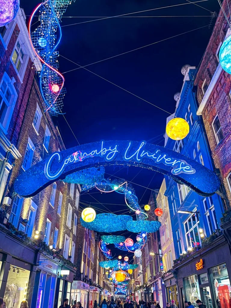 carnaby universe neon sign hanging above the street that is lined with other bright decorations