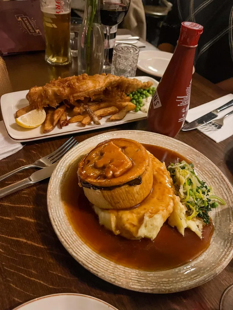 a fish and chips dish, and a steak and ale pie on the table at the lamb and flag pub in london
