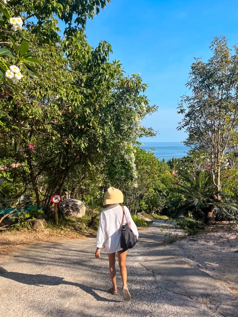 woman walking downhill on a paved road towards the ocean in koh tao, thailand