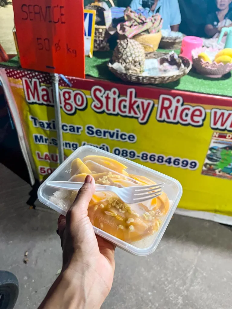 hand holding a plastic container with mango sticky rice to go from a local street food stand in koh tao, thailand