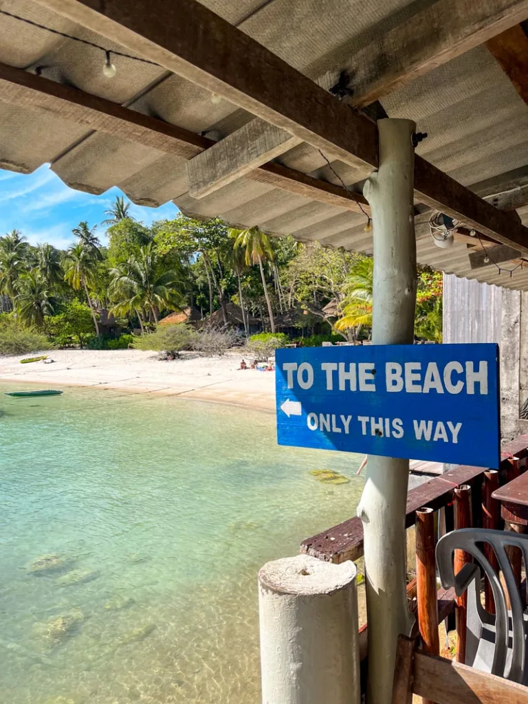 wooden sign signaling to the beach, with a view of a beach in koh tao thailand
