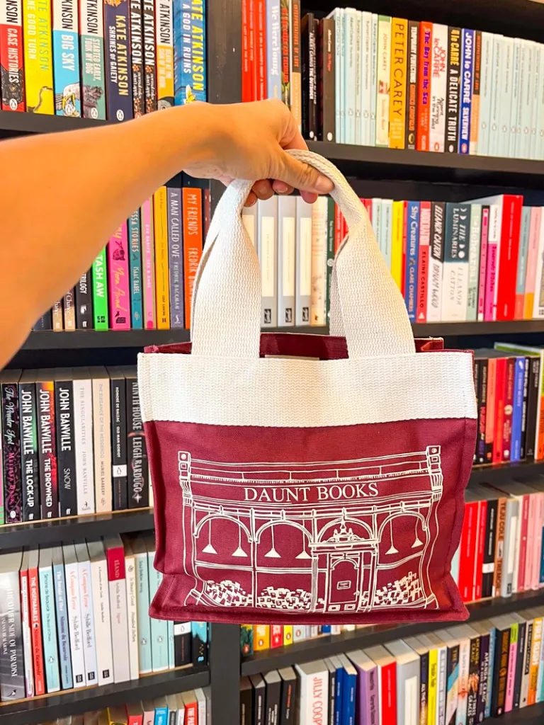 hand holding a burgundy mini tote of daunt books at the shop in notting hill, london