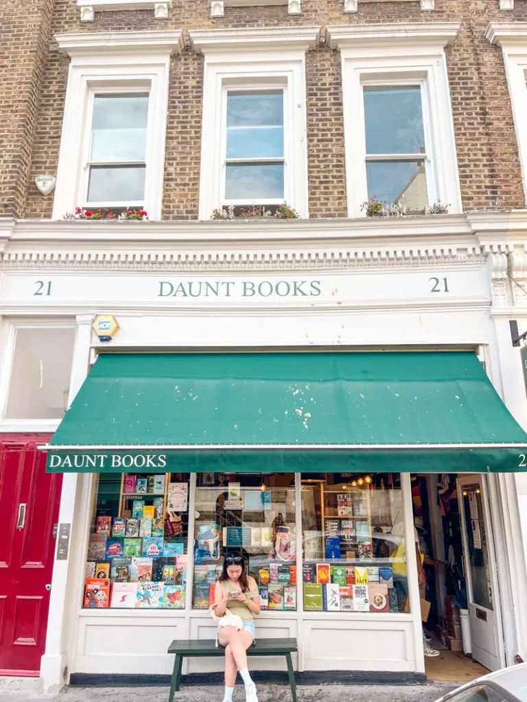 woman sitting on a bench outside daunt books shop in notting hill, london