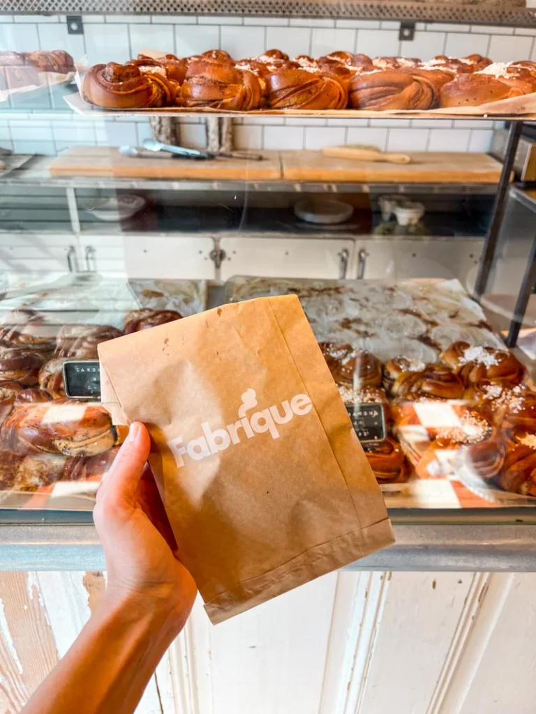 hand holding a pastry bag infront of a display of cardamom buns at fabrique bakery in notting hill, london