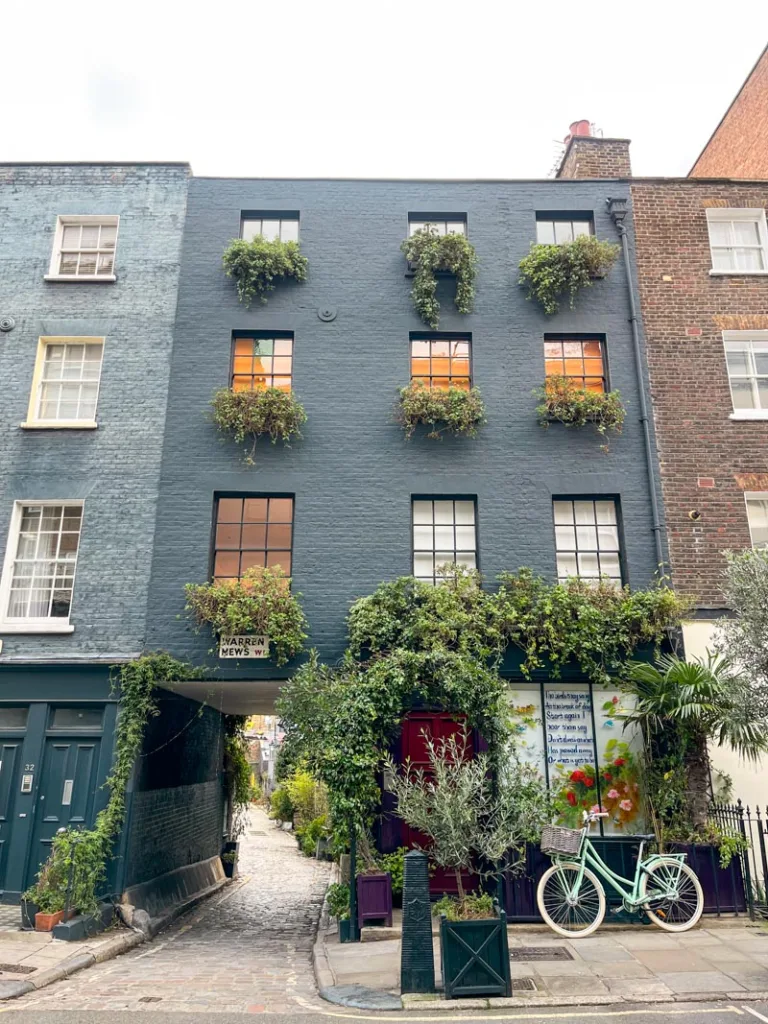 dark gray building with greenery on every windown and an entrance to warren mews in fitzrovia, london