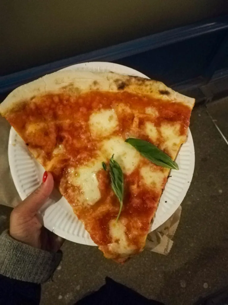 hand holding a paper plate with a margherita pizza slice from homeslice, one of the best cheap places to eat in london