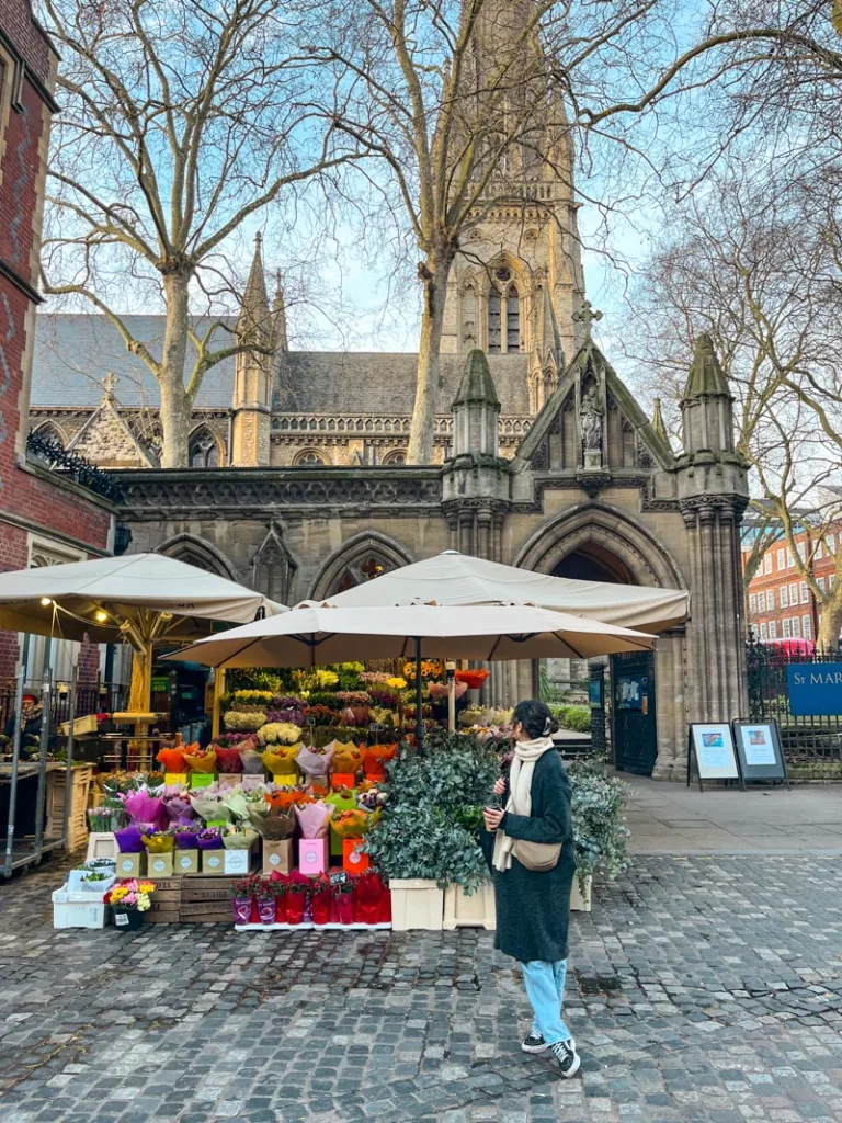 woman standing in front of a flower stand in kensington high street, london