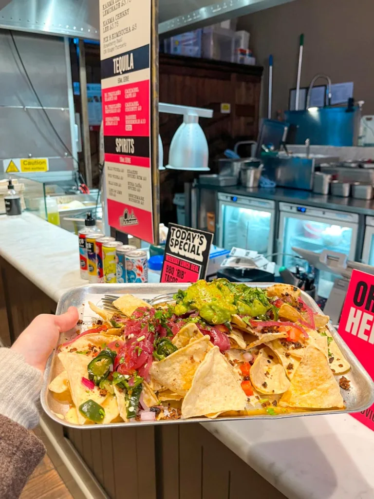hand holding a metal tray of nachos from club mexicana at mercato mayfair in london