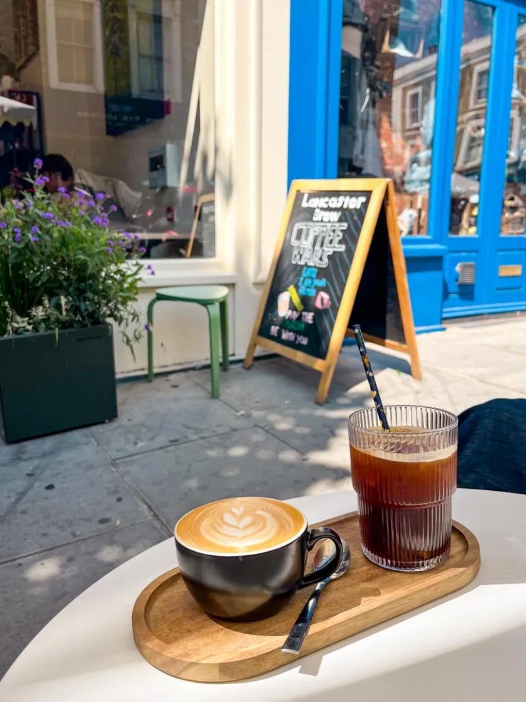 a latte and an iced americano on a wooden tray on a table outside lancaster brew in notting hill, london
