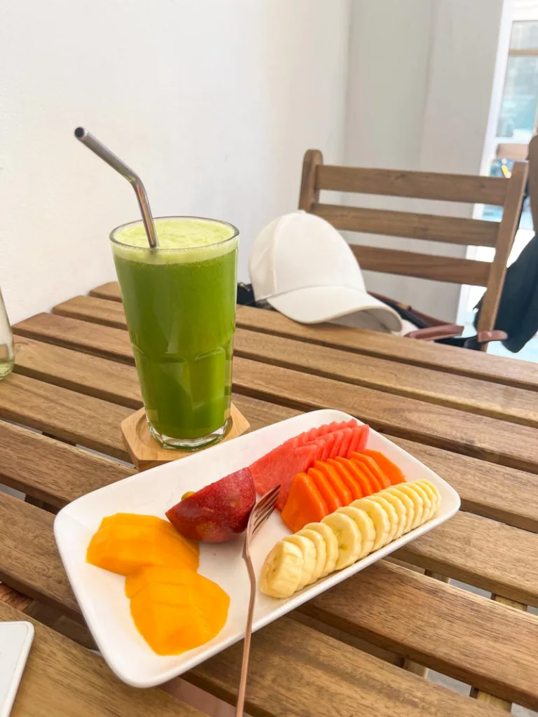 a fruit plate and a green smoothie on a small wooden table at living juices in koh tao