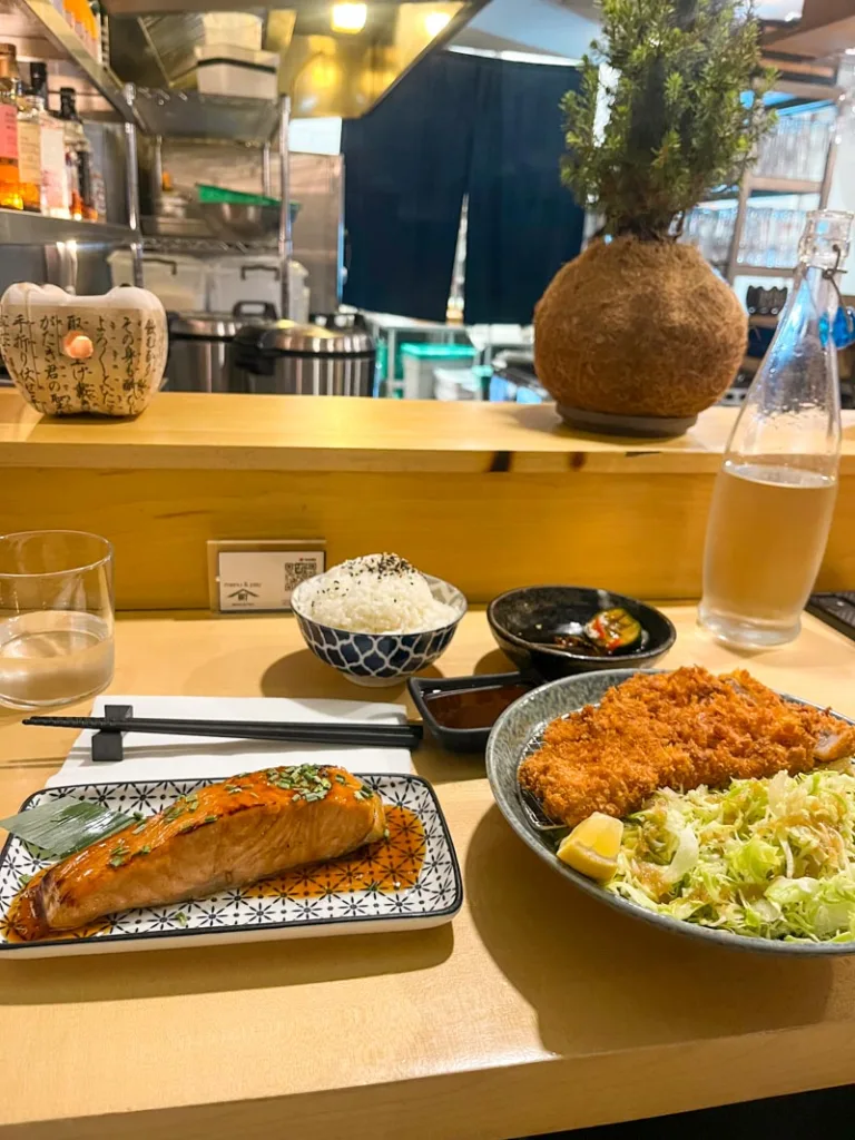 a salmon steak, a tonkatsu plate, and a bowl of rice on a bar at mashiya restaurant in london