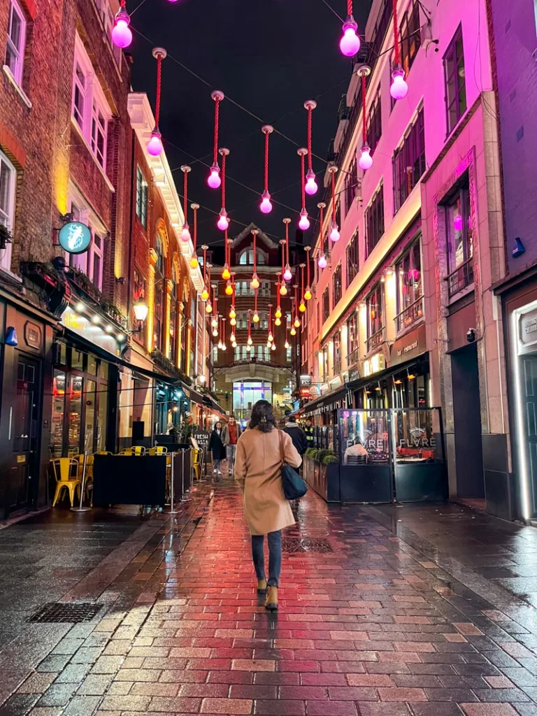 woman walking on a street in soho, london, with bright pink light decorations hanging above