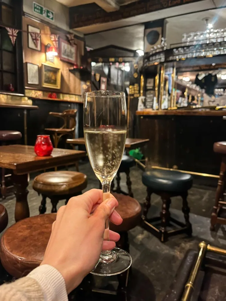 hand holding a glass of prosescco in a dark wooden bar at the lamb and flag pub in london